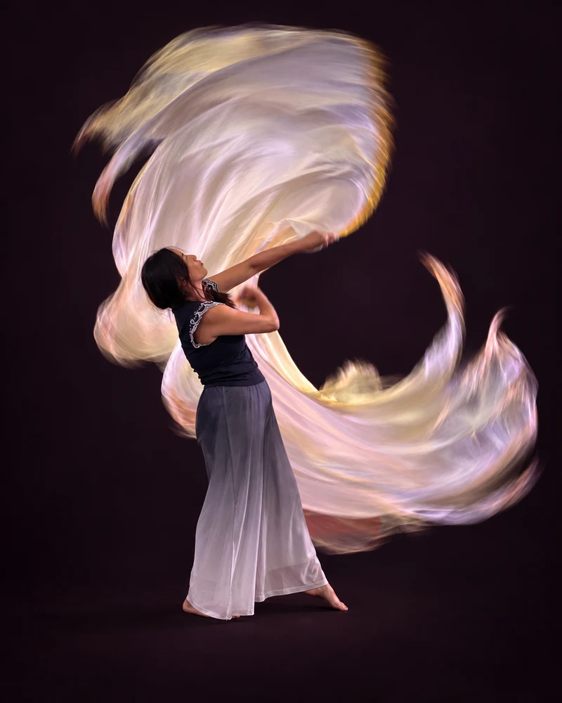Woman worshipping with flowing pale silk flags against a dark aubergine background.